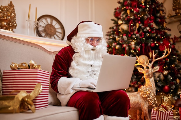 Babbo natale seduto a casa sua e leggendo la posta elettronica sul laptop