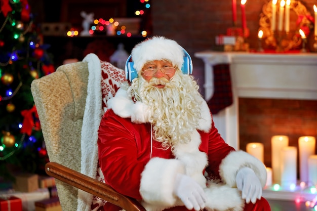 Babbo natale seduto con le cuffie seduto su una comoda sedia a dondolo a casa