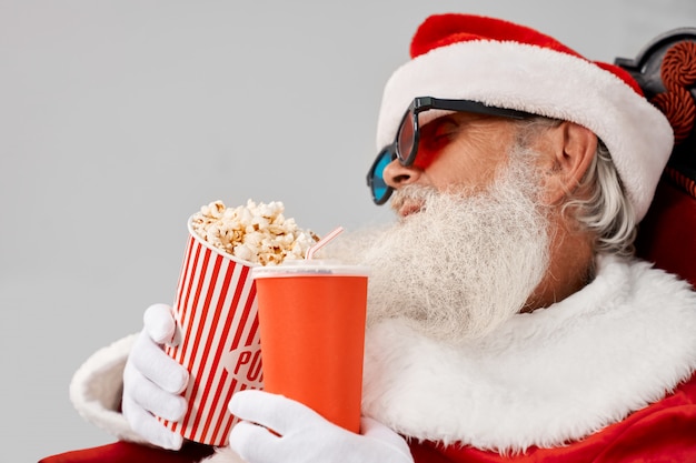 Foto babbo natale che dorme in poltrona con popcorn e cola