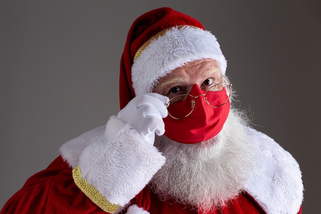 빨간 코비드-19 안전 마스크 뒤에 산타클로스가 웃고 있다. 사회적 거리두기가 있는 크리스마스.