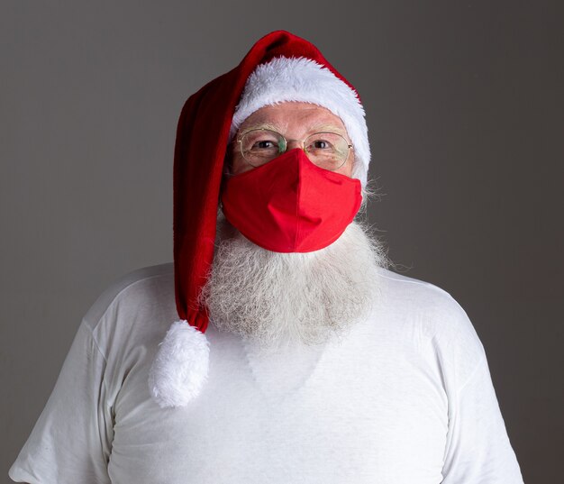 Photo santa claus smiles behind red covid-19 safety face mask. christmas with social distance.