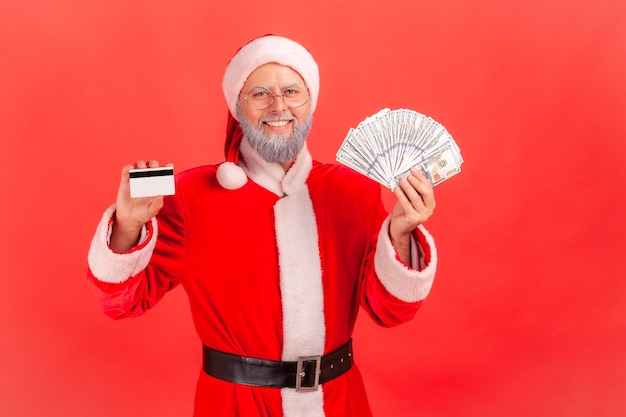 Photo santa claus standing holding fan of dollars and showing credit card, cashback.