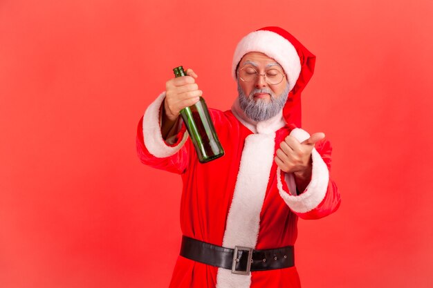 Santa claus standing with beer bottle, being drunk, standing with closed eyes and showing thumb up.