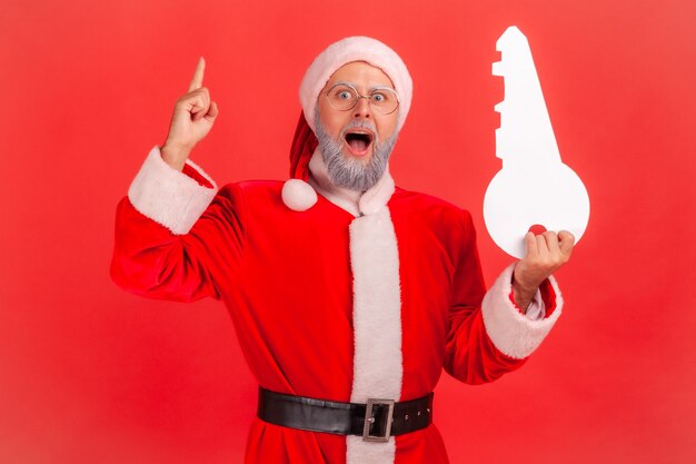 Santa claus standing with open mouth, holding paper key, has idea for buying property.