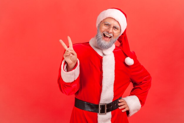 Santa claus standing with raised hands and showing v sign or peace, victory gesture.