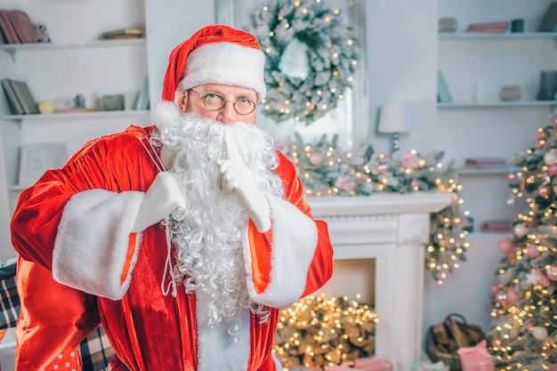 Santa Claus stands near a fireplace with sack of gifts