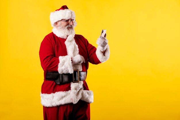 Santa claus taking a selfie with a mobile phone on a yellow background