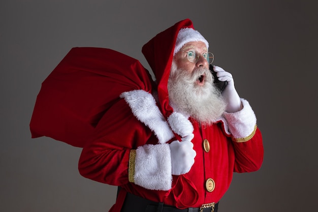 Photo santa claus using a smartphone. surprised.