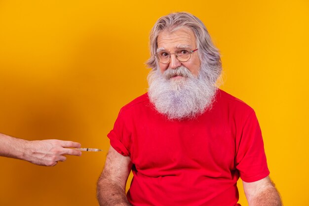 Santa Claus wearing face mask getting vaccinated with injection. elderly man vaccinating on free background for text.