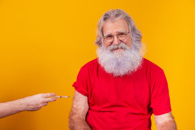 Santa Claus wearing face mask getting vaccinated with injection. elderly man vaccinating on free background for text.