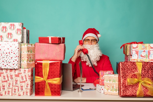 Santa Claus wearing hat work in his oficce with presents, preparing for holidays.