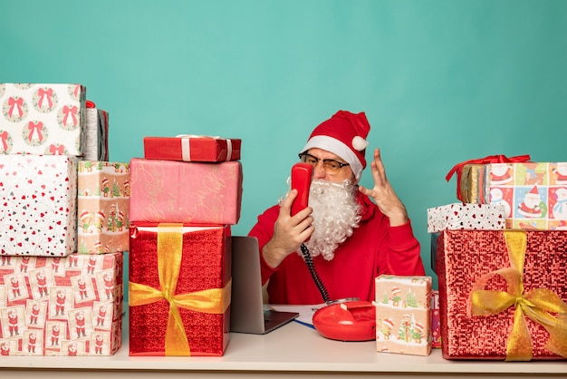 Babbo natale che indossa un cappello lavora nel suo ufficio con i regali, preparandosi per le vacanze.