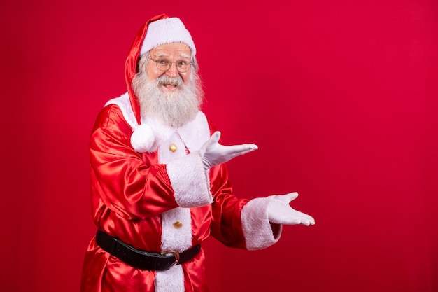 Santa Claus wijzend opzij, reclame kerstpromotie, Nieuwjaar kerst korting advertentie geïsoleerd op rode achtergrond.