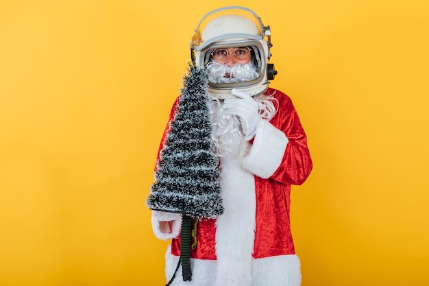 Santa Claus with astronaut helmet holding a Christmas tree on yellow