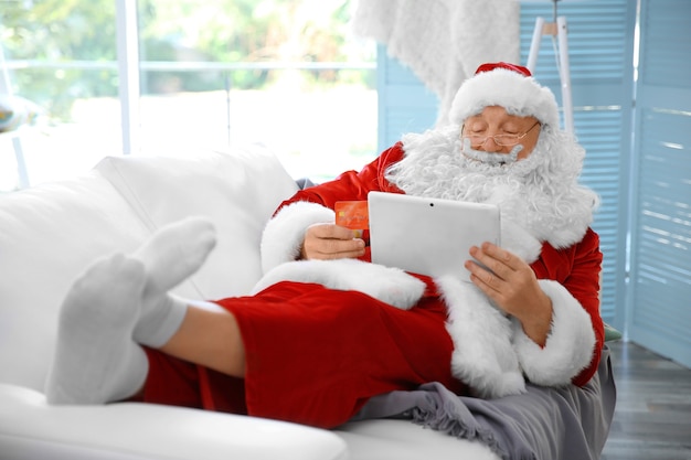 Santa Claus with credit card and tablet on couch at home