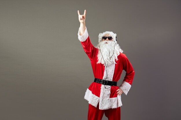 Santa Claus with a long white beard in sunglasses and headphones listen a rock music