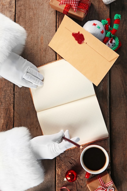 Photo santa claus writes in notebook on wooden surface