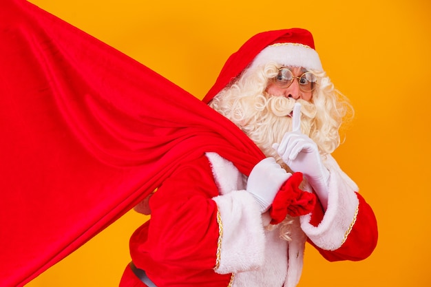 Santa Claus on yellow background holding bag with gifts with free space for text behind his back. christmas campaigns