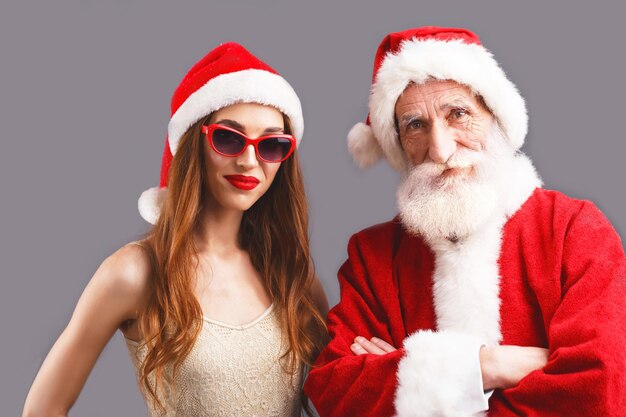 Santa Claus and young mrs Claus wearing Santa hat and sunglasses standing on the gray background