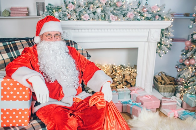 Santa claus zit in de buurt van een open haard met geschenkdozen