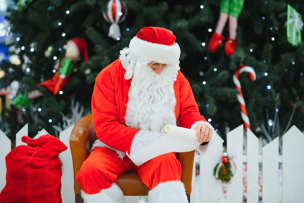 Santa Claus zittend op de achtergrond van de kerstboom in de lobby van het moderne winkelcentrum. Bokeh basisachtergrond voor ontwerp.