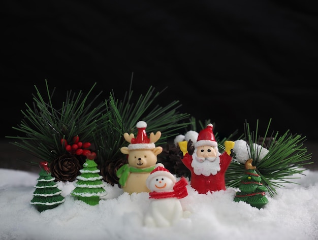 Santa Clause and friends sitting on white snow with blurred Christmas trees on black background to c