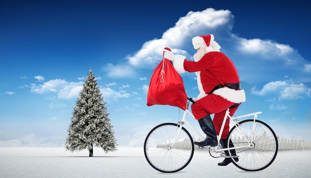 Санта катается на велосипеде и держит мешок у елки в снежном пейзаже