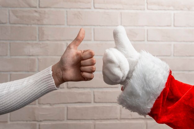 Santa and the girl give a thumbs up on the background of a light brick wall