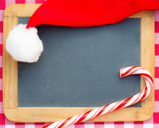 サンタの帽子とクリスマスのキャンディーフレームのヴィンテージ黒板ブランク。 Wintarの休日の概念