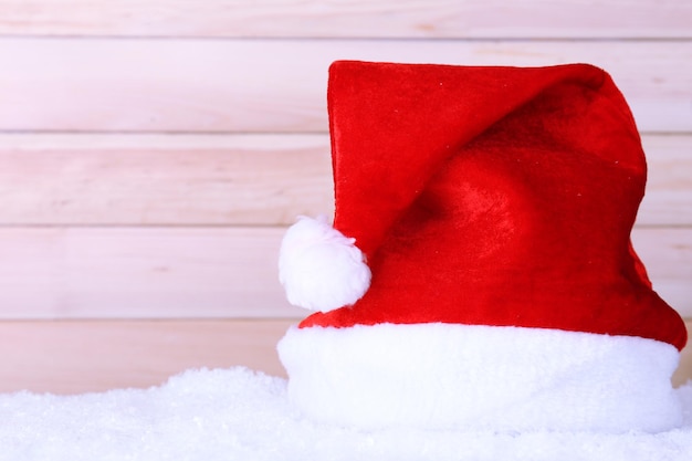 Santa hat on snow on color wooden background