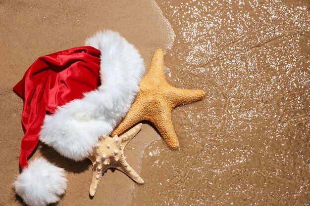 Шляпа Санты с морскими звездами на пляже. Концепция праздника Рождества