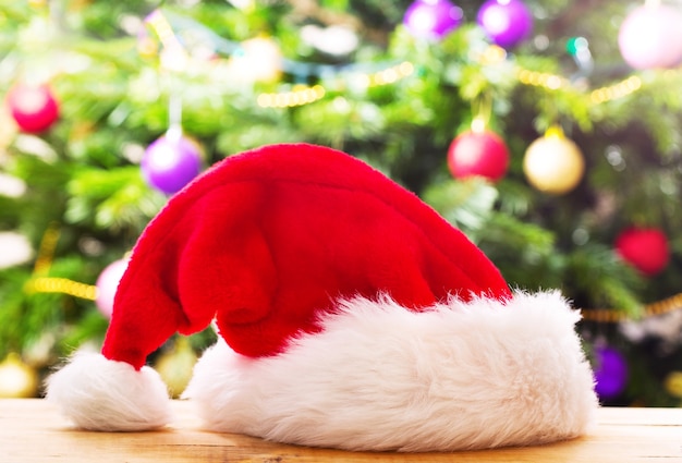 Santa hat on wooden table against christmas tree