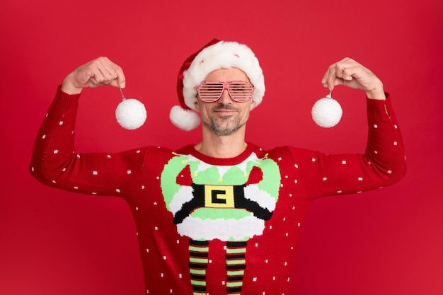 Santa hold christmas ball Portrait of middle aged man in sweater isolated over red background Concept of holidays happiness emotions and Christmas celebration