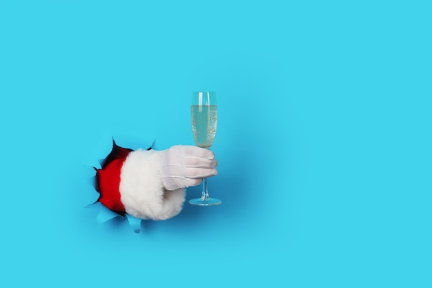 Santa Holding Champagne Flute geïsoleerd over lichtblauw. Alleen hand en arm