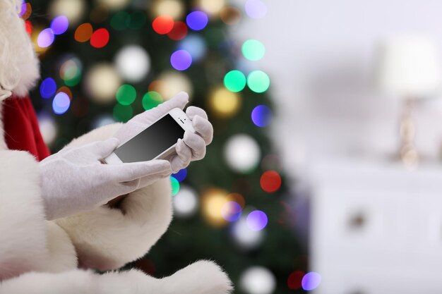 Babbo natale che tiene il cellulare sullo sfondo dell'albero di natale