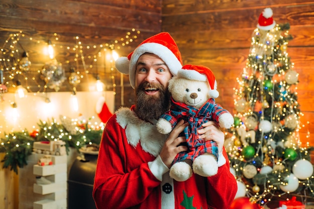 Santa man poseren met teddy op vintage houten achtergrond gelukkig santa gekleed in winterkleding dun...