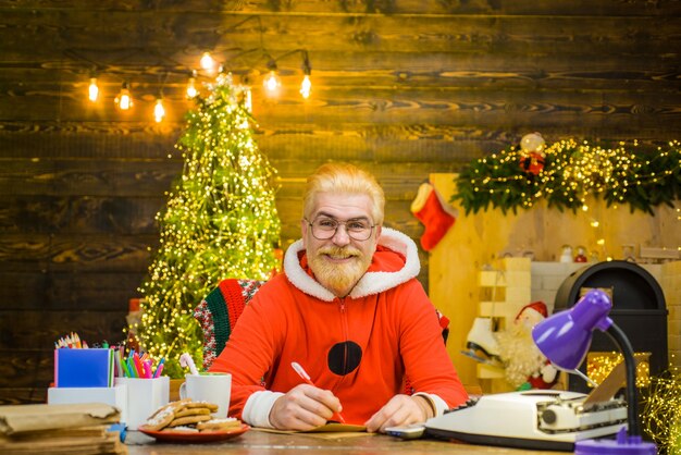 Санта человек санта клаус сидеть за столом новый год фон рождественские украшения улыбается санта клаус
