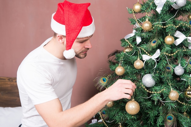 Santa man versieren kerstboom met gouden snuisterij. Feestelijke decoraties en ornamenten concept. kerstmis, nieuwjaar, vooravond, vakantievoorbereiding, feest.