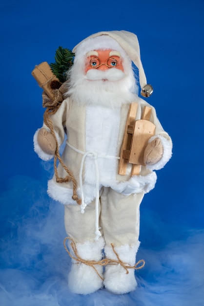 Santa puppet doll with wooden sleigh against blue with misty smoke