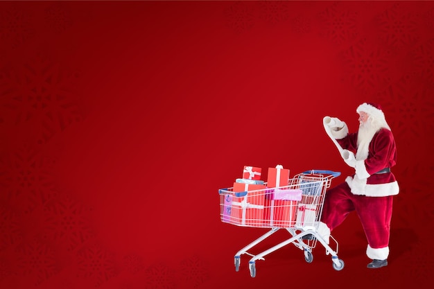Santa pushes a shopping cart while reading against red background