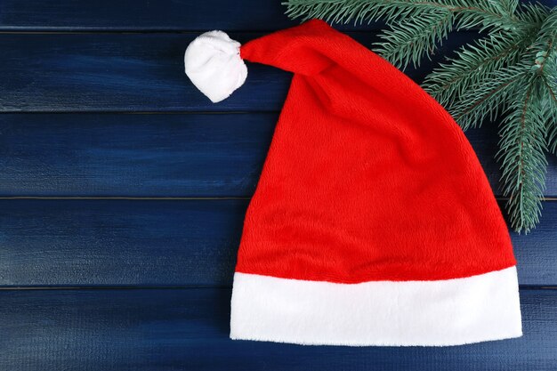 Photo santa red hat with branch of fir-tree on color wooden surface