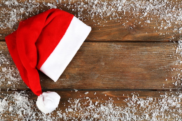 Cappello rosso di babbo natale con fiocchi di neve su fondo in legno