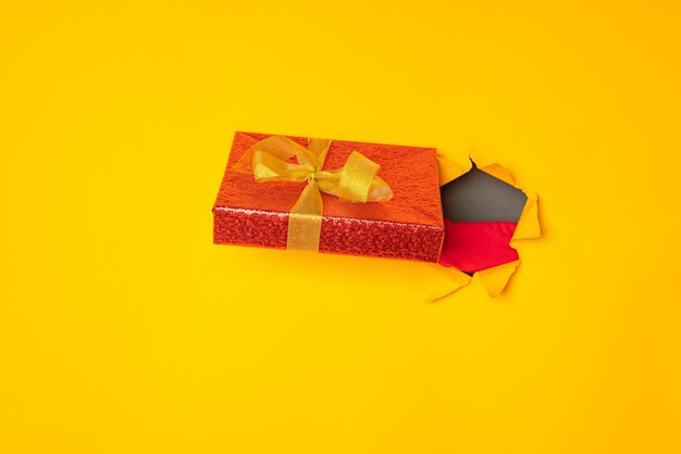 Santa's hand holding a box with a gift in the hole yellow background