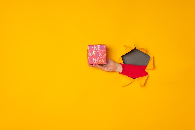 Santa's hand holding a box with a gift in the hole yellow background