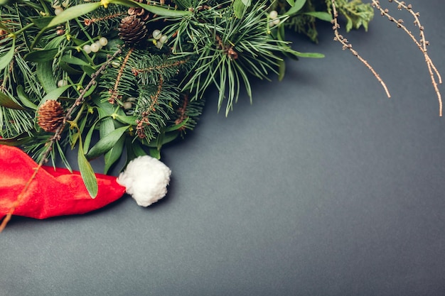 円錐形のモミ、松、ヤドリギの枝によって置かれたサンタの帽子。灰色の背景にクリスマスと新年の装飾。スペース