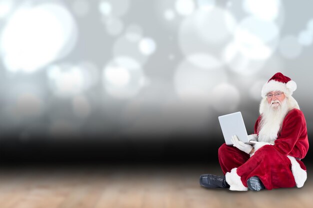 Santa sits and uses a laptop against shimmering light design over boards