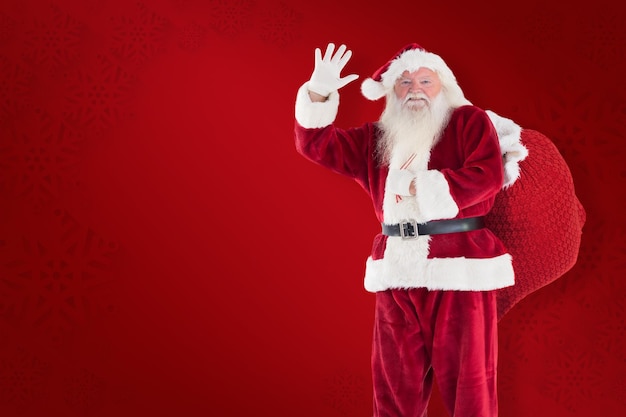 Santa waves to the camera against red background