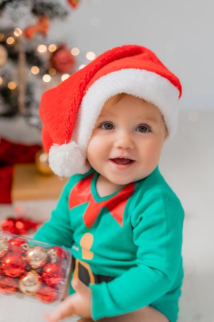 Santas kleine helper naast de kerstboom met kerstballen in zijn handen portret van baby