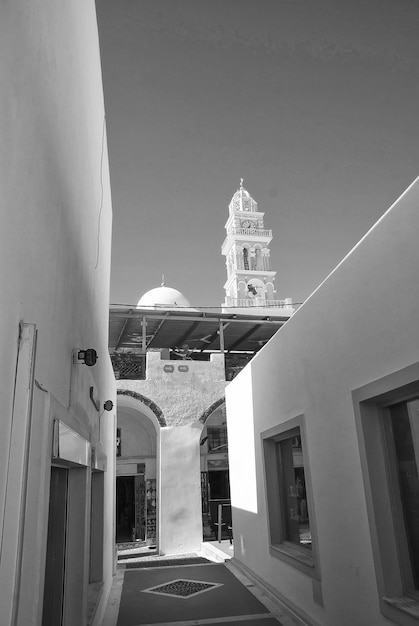 Santorini Griekenland straat met gebouw en huis bij klokkentoren met klok op blauwe hemelachtergrond