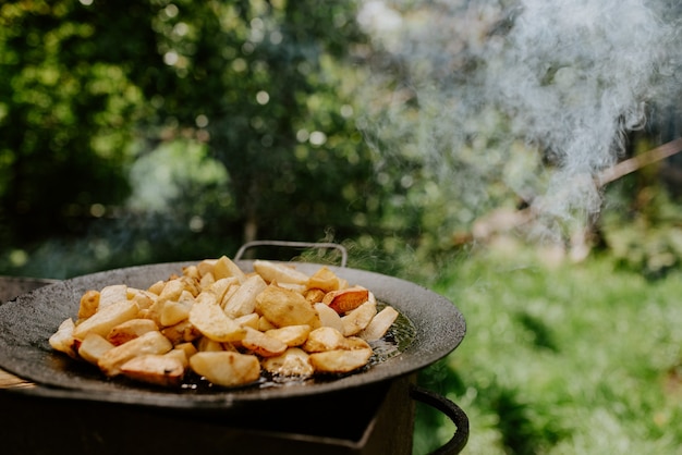 Sappige gebakken aardappelen met een korst gekookt in een grote zwarte pan op de grill. wazige achtergrond